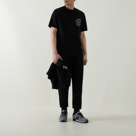 Model wearing Hugo black cotton crew neck T-shirt with chest patch detail, styled with black trousers and grey trainers.