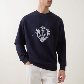 Model wearing Hugo dark blue cotton crew neck sweatshirt with white floral crest embroidery on chest, styled with white trousers