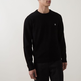 Model wearing Hugo black crew neck knit jumper with small logo badge on chest, paired with black trousers