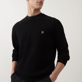 Model wearing Hugo black crew neck knit with small logo patch, long sleeves, styled with dark trousers