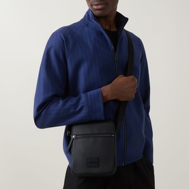 Model carrying Hugo Ethon 2.0 Crossbody Bag in black, pebble texture, silver-tone hardware, adjustable strap, worn cross-body with blue jacket