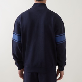 Model wearing Hugo dark blue cotton half zip sweatshirt, back view, with blue stripe detail on sleeves, styled with matching navy trousers.