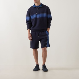 Model wearing Hugo dark blue cotton half zip sweatshirt with blue stripe detail, styled with matching navy drawstring shorts and dark trainers.
