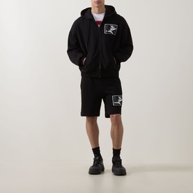 Model wearing Hugo black zip-up hoodie with graphic chest print, styled with matching black shorts and black chunky trainers.