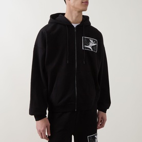 Model wearing Hugo black zip-through hoodie with embroidered bird graphic patch on chest, styled with matching black joggers.