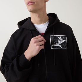 Model wearing Hugo black zip-up hoodie with graphic chest patch, styled over white crew-neck tee