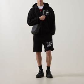 Model wearing Hugo black cotton hoodie with zip, styled with matching black shorts, crossbody bag and black chunky trainers.
