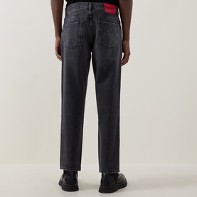 Model wearing Hugo 3049 silver grey straight-leg jeans, rear view, with red label detail at waistband and black shoes.