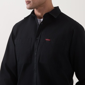 Model wearing Hugo Egrin Logo Overshirt in black, showing red embroidered logo, chest pocket, and pointed collar. Layered over white tee.