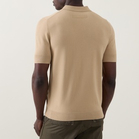 Model wearing Hugo San Peter-CV Knitted Polo Shirt in Medium Beige, rear view showing ribbed trims and straight hem, styled with olive trousers.