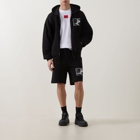 Model wearing Hugo black cotton shorts with logo patch, styled with matching black zip-up hoodie, white tee and black chunky trainers