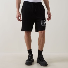 Model wearing Hugo black cotton shorts with graphic logo patch, styled with black socks and chunky trainers