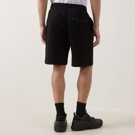 Model wearing Hugo black cotton sweat shorts, shown from behind, styled with black socks and chunky trainers