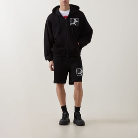 Model wearing Hugo black cotton shorts with graphic print, styled with matching black zip-through hoodie and black trainers