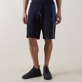 Model wearing Hugo dark blue cotton shorts with side snap-button stripe detail and drawstring waist, styled with blue trainers