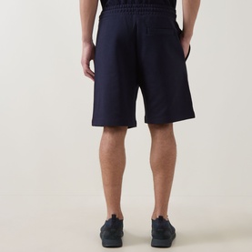 Model wearing Hugo dark blue cotton shorts, rear view, styled with navy trainers