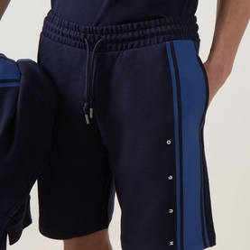 Model wearing Hugo dark blue cotton shorts with contrast blue side stripe and logo detail, paired with matching joggers.