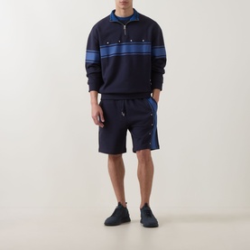 Model wearing Hugo dark blue cotton shorts with side button detail, styled with matching navy striped sweatshirt and dark trainers.
