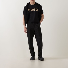 Model wearing Hugo black tailored trousers in wool-polyester blend, styled with a black HUGO logo T-shirt and black trainers.