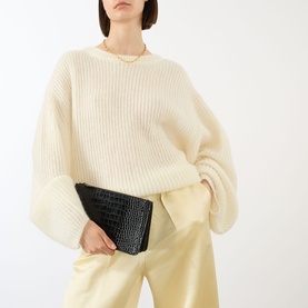 Model carrying Toteme Threefold Croco-Embossed Clutch in black with gold-tone hardware; styled with cream ribbed knit and pale yellow trousers