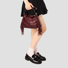 Model carrying Maje bag in burgundy leather with fringe detail and gold-tone hardware, styled with black mini skirt and loafers