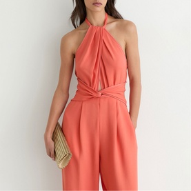 Model wearing Reiss coral pink halterneck jumpsuit with gathered neckline and wide-leg trousers, styled with a woven clutch bag