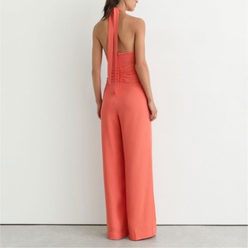 Model wearing Reiss coral pink halterneck wide-leg jumpsuit, shown from the back with ruched bodice detail