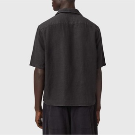 Model wearing All Saints jet black short-sleeve linen shirt, back view, styled with matching black trousers.