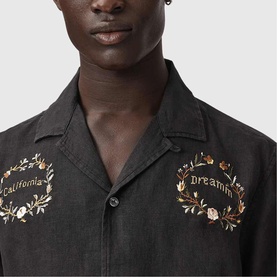 Model wearing All Saints jet black shirt with floral wreath and California Dreamin' embroidery detail, open collar