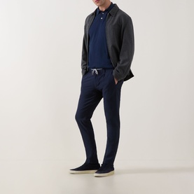 Model wearing Eleventy Iconic Navy Polo Shirt with grey overshirt, navy trousers and navy canvas shoes.