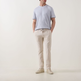 Model wearing Eleventy Iconic Garment-Dyed Trousers in sand, tapered leg with pressed creases, styled with light blue T-shirt and cream trainers.
