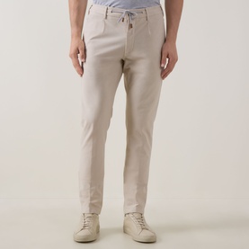 Model wearing Eleventy Iconic Garment-Dyed Trousers in sand, tapered-leg with drawstring waist, styled with cream trainers
