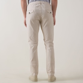 Model wearing Eleventy Iconic Garment-Dyed Trousers in sand, rear view showing tapered leg, rear flap pockets with button closure and pressed creases.
