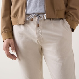 Model wearing Eleventy Iconic Garment-Dyed Trousers in sand, tapered leg with drawstring waist, styled with a tan bomber jacket.