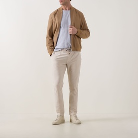 Model wearing Eleventy Iconic Garment-Dyed Trousers in sand, tapered leg with pressed creases, styled with tan bomber jacket and light blue tee.
