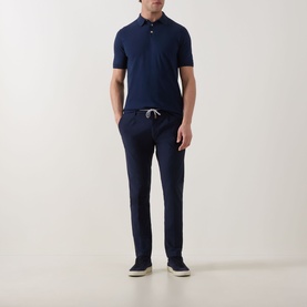 Model wearing Eleventy navy trousers with drawstring waist, styled with a navy polo shirt and cream trainers.