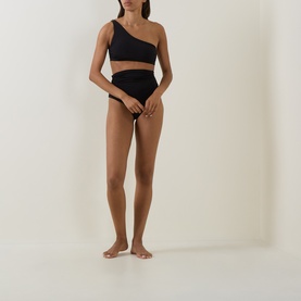 Model wearing Max Mara black bikini brief with matching one-shoulder crop top, full-length front view on plain background.