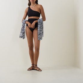 Model wearing Max Mara black bikini brief with matching one-shoulder top, styled with pearl necklace, zebra-print cover-up and brown strappy sandals.