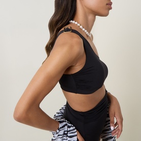 Model wearing Max Mara black bikini top with ruched detailing, styled with zebra-print bottoms and a pearl necklace.