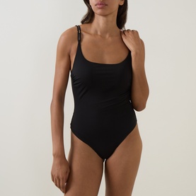 Model wearing Max Mara black swimsuit with scoop neck, ruched sides, and thin braided straps.
