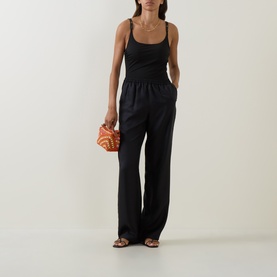 Model wearing Max Mara black swimsuit styled with wide-leg black trousers, carrying a small orange clutch bag, with flat sandals.