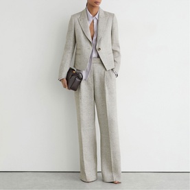 Model wearing Reiss beige tailored blazer and wide-leg trousers, styled with a white shirt, grey knit and small dark brown shoulder bag.