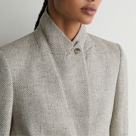 Model wearing Reiss beige herringbone jacket, close-up detail showing collar and gold button fastening.
