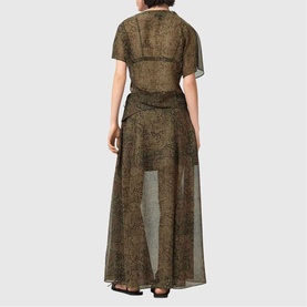 Model wearing All Saints Sali Printed Flared Skirt in Sirius Gold, maxi length with sheer overlay, side tie detail, back yoke, short-sleeve top.