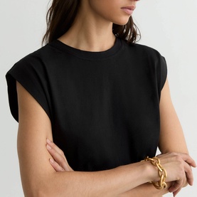 Model wearing Reiss black sleeveless top with padded shoulders, arms crossed, styled with a gold chunky chain bracelet