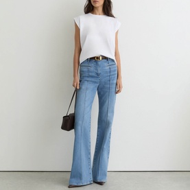 Model wearing Reiss white sleeveless top with light blue wide-leg flare jeans, gold belt, and black shoulder bag.