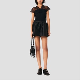 Model wearing Maje red mini dress with sheer lace top, styled with black loafers and carrying a black fringed bag