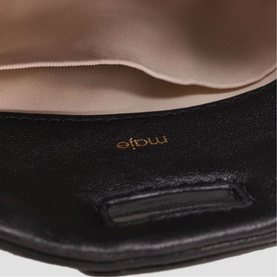 Maje red bag interior detail showing pink satin lining and gold brand logo stamp on black leather base.
