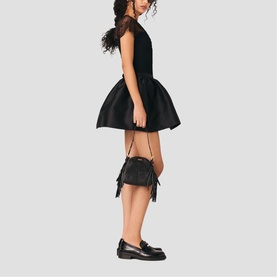 Model carrying Maje red crossbody bag with fringe detail, styled with black mini dress and loafers