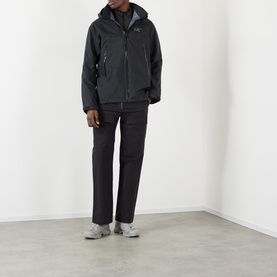 Model wearing black zip-up hooded technical jacket styled with matching black trousers and grey trainers